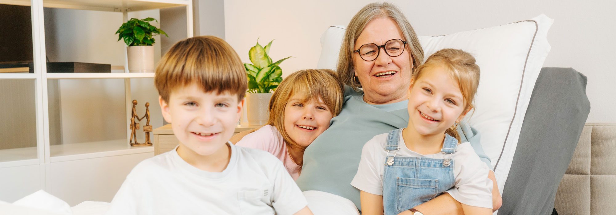 Ältere Frau im Pflegebett mit drei lachenden Enkelkindern