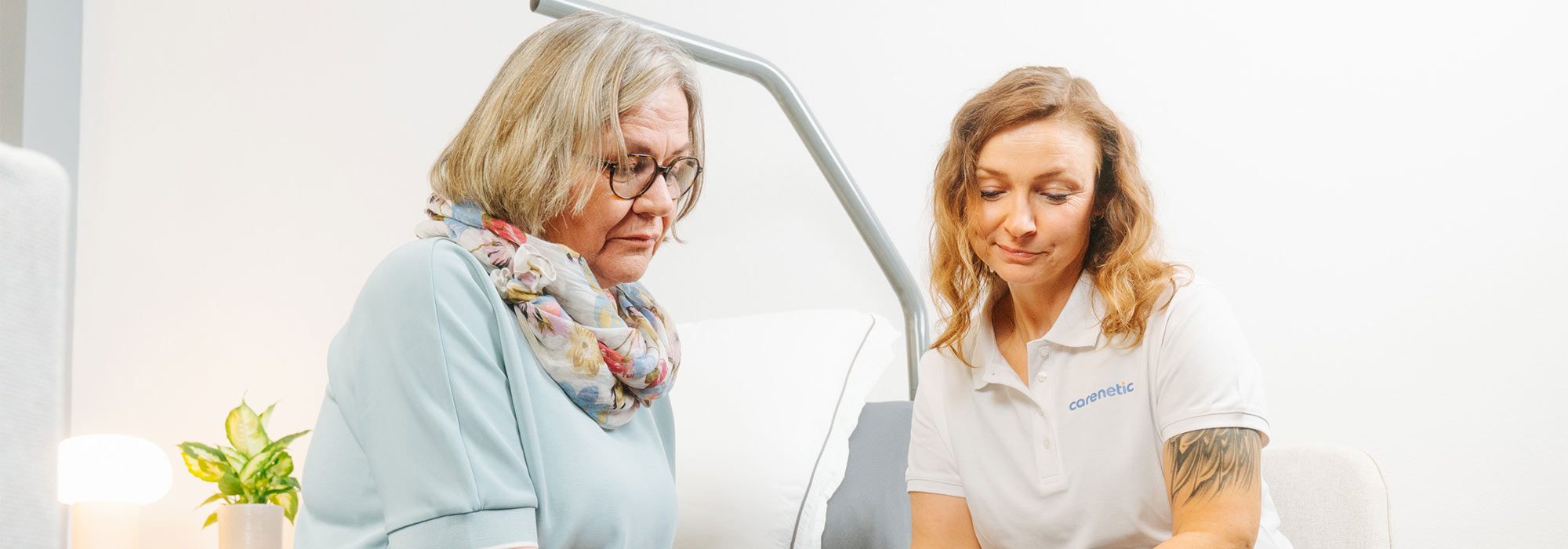 Carenetic Mitarbeiterin im Gespräch mit einer Patientin am Pflegebett